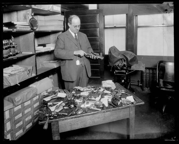A Seattle police staff member checks tagged firearms and other evidence in a property room around 1922.